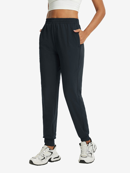Model with hand in pocket wearing lightweight women's stretchy joggers sweatpants in dark grey.