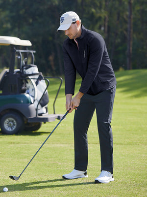 Model in navy softshell water resistant lightweight jacket preparing to tee off, full-body shot
