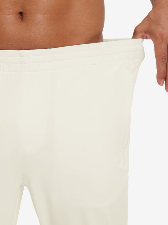 Model stretching waistband to show fit of lightweight traning track pants in cream.