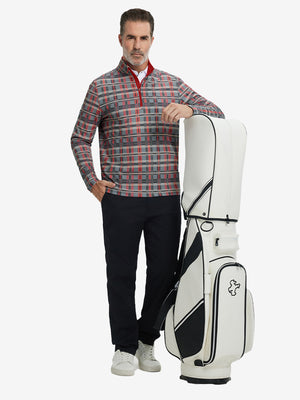 Full-body shot of model holding golf bag, dressed in full print quarter zip pullover in red/black/white plaid.