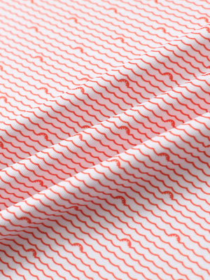 Close-up of orange sea wave performance print boys golf polo fabric showing moisture-wicking texture and vibrant pattern.