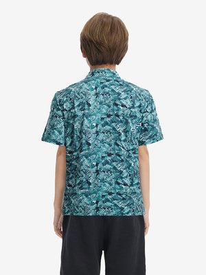Back half-body view of youth wearing dark green leaf performance print boys golf polo, showing rear design