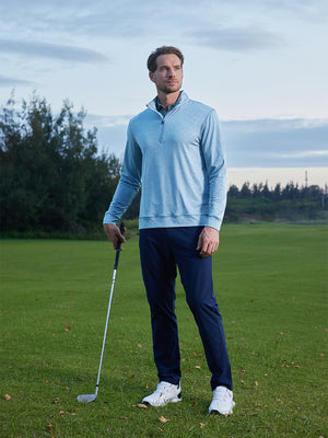 Model on grass under blue sky, leaning on golf club, wearing quarter zip melange pullover in light blue melange.